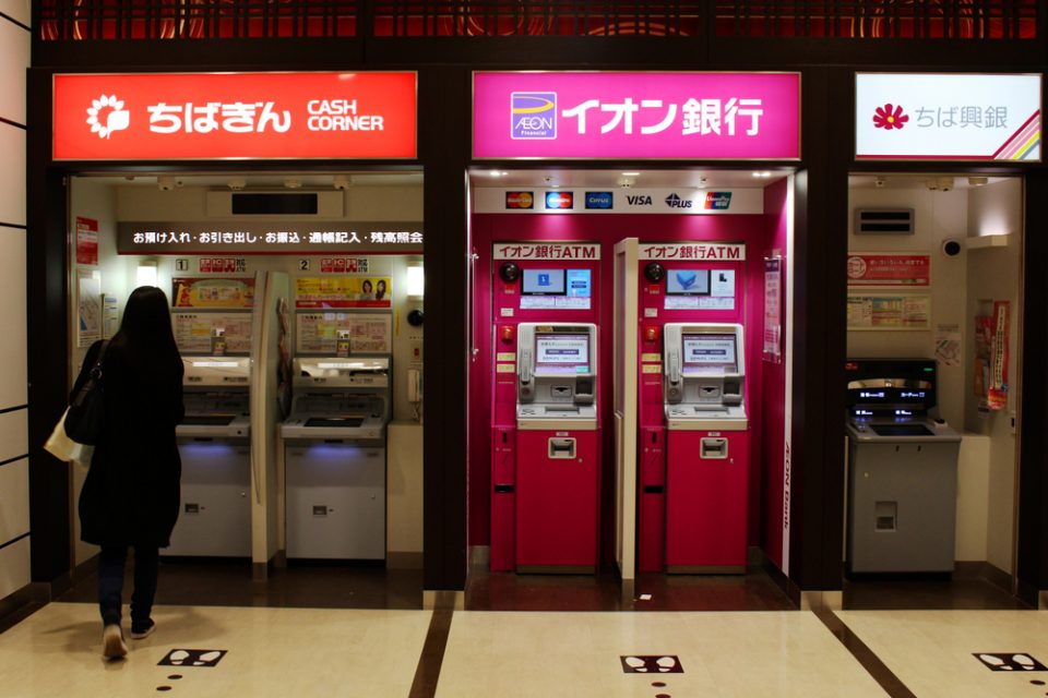 A customer approaches a row of ATMs (including Chiba Ginko and Aeon Ginko) in an Aeon Mall in Makuhari.